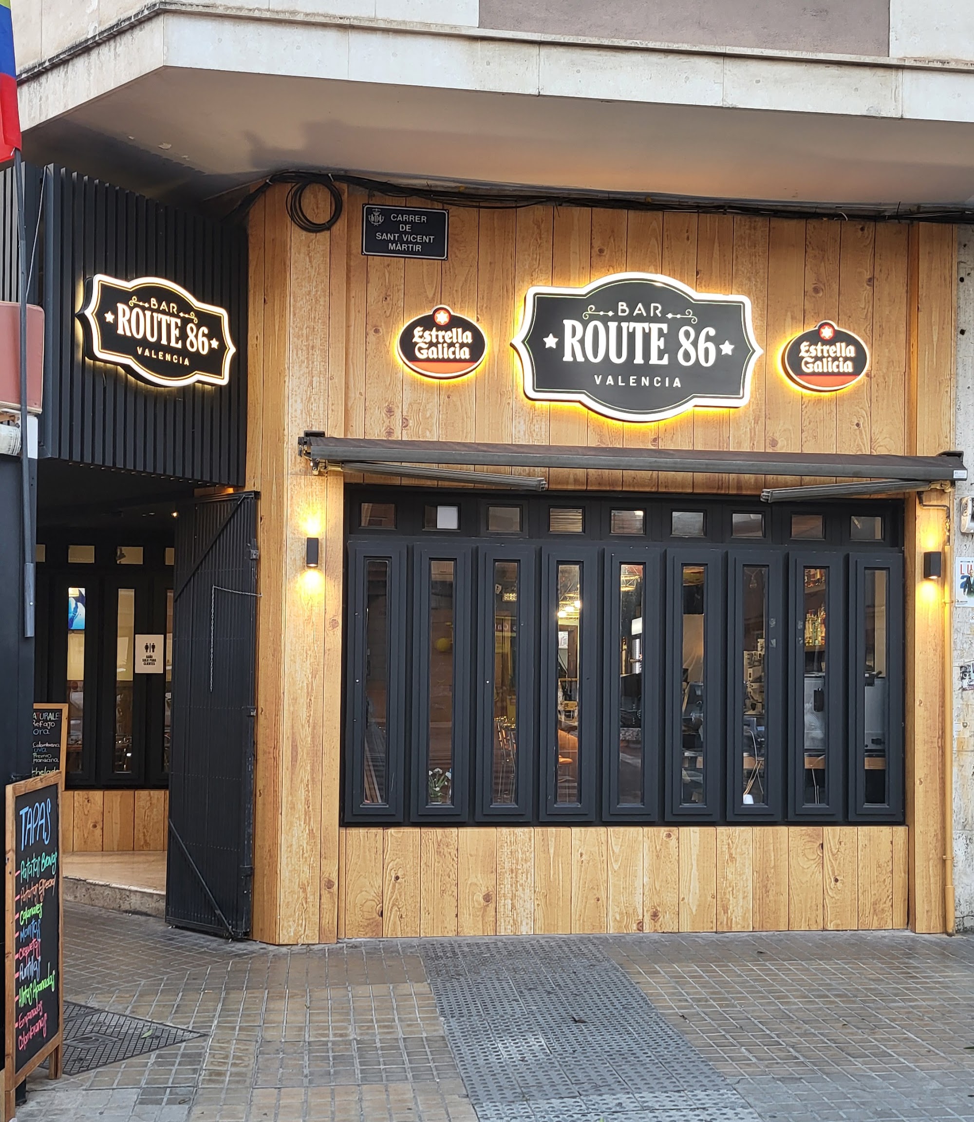 Fachada de Bar Route86 Valencia — madera, metal negro y luces cálidas
